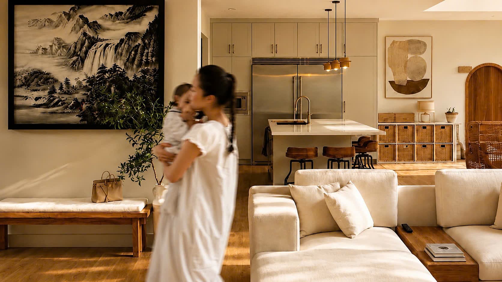 A mother holding her baby in a warm, sunlit open-plan living and kitchen space